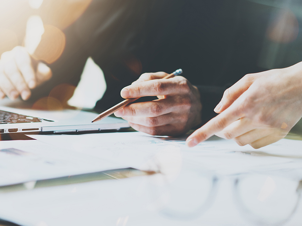 ノートパソコンと書類を使って作業をする手元の写真